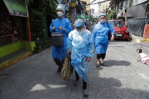 MANILA. In this photo taken in May 2021, health workers in protective suits walk to the homes of residents who are not able to go to vaccination centers in Manila. (File)