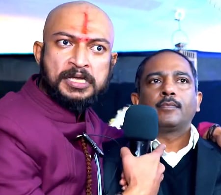 पादरी से धमकाने वाले अंदाज में बात करते हुए सत्यनिष्ठ आर्य (बायें)