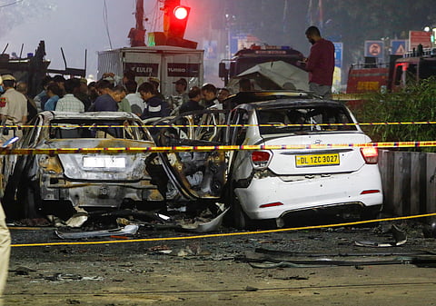 Police personnel stand near the charred remains of vehicles at the site of a car blast near Gate No. 1 of the Red Fort Metro Station, in New Delhi.