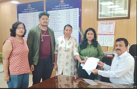 Four individuals from the Karnataka IT union submit a memorandum to the labour commissioner, standing around a table with documents.