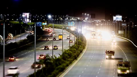 Vehicles on the Outer Ring Road around Hyderabad at night. There are many vehicles on either side of the road with their headlights and taillights glowing, and a divider in between filled with plants. 