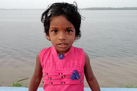 Child in pink dress standing in front of a water body.