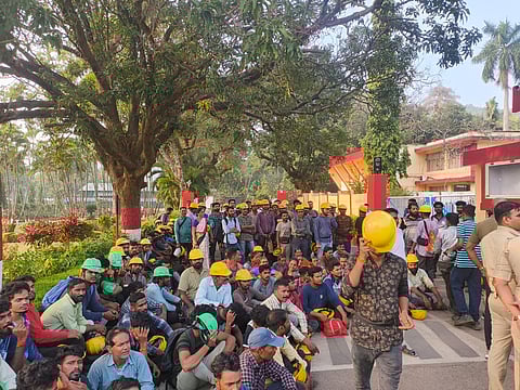 A group of protesters wearing construction caps sit along the roadside near the Grasim Industrial plant in Karwar.