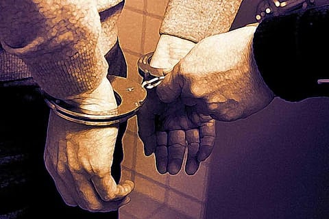 Close-up image of a person's hands in handcuffs being secured by another individual, with a warm-toned background. 
