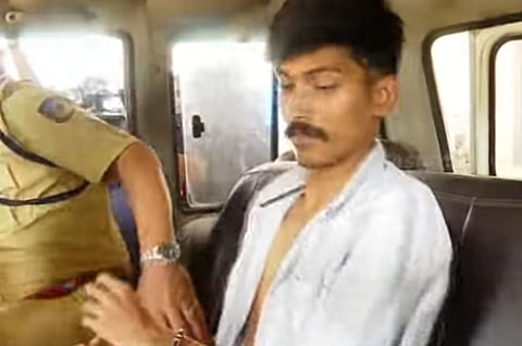 Ashik sitting in the back of a police vehicle with handcuffs, accompanied by a police officer
