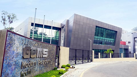Modern school building of GEMS Modern Academy, Kochi, featuring sleek architecture, glass windows, and a landscaped entrance with a prominent signboard. 