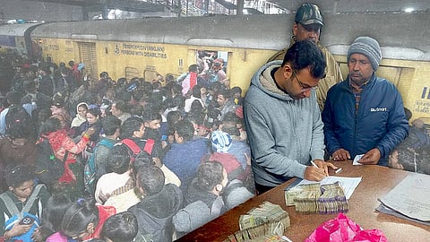 A stylised image of the stampede site at New Delhi Railway station. In the background, a large crowd jostling forward to enter a stopped train. In the foreground on the right end of the image, a family member of a victim being handed over cash. Wads of cash can be seen on the table next to him.