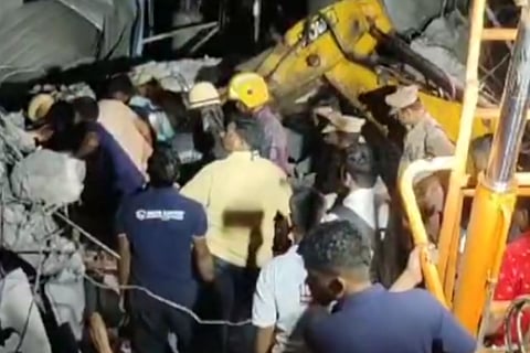 Group of men surrounded by rubble. A JCB deployed to excavate the rubble.