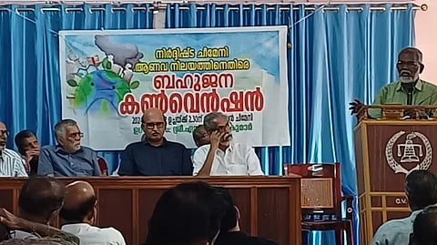 Anti-nuclear activist SP Udayakumar standing at the podium and speaking as he inaugurates a convention against the proposed nuclear power plant at Cheemeni in December 2024; six other men are seen sitting on the stage while some people are visible in the audience.