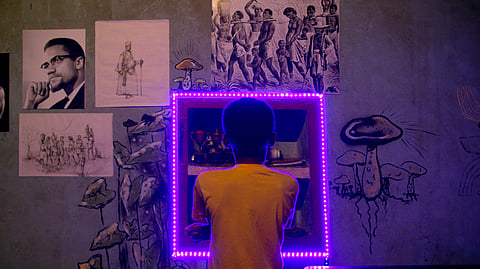 The image shows a boy with his back to the viewer, looking through pictures on a wall which is lit up by a strip of fairy lights.