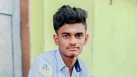 The victim, Class 12 Dalit student Devendra Raj, is seated on a step,dressed in his blue school uniform. There is pale blue door and a green wall behind him.