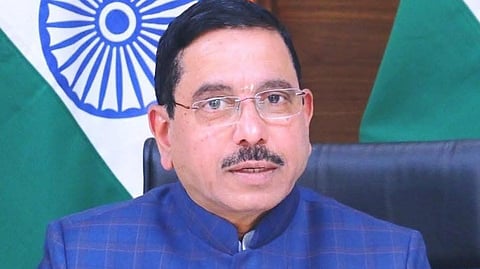 Pralhad Joshi in a blue checkered jacket sitting in front of an Indian flag.