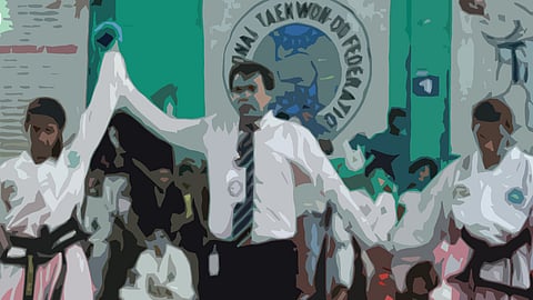 A referee in a white shirt and tie raises the arm of a martial artist in a white dobok with a black belt, signaling victory in a Taekwondo match. Another competitor stands on the other side. The background features a crowd and a large banner with the words 'Taekwondo Federation.'