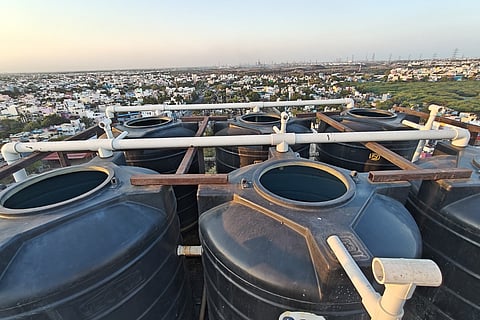Water tanks without lids, connected to pipes on the terrace of a building.
