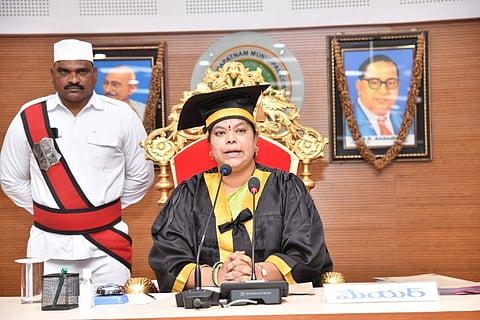 Visakhapatnam Mayor Golagani Hari Venkata Kumari dressed in ceremonial robes and a graduation-style cap sits on an ornate golden chair, speaking at a podium with microphones. She is identified as the mayor by a nameplate in Telugu reading 'Mayor'. A uniformed security guard stands behind her. Portraits of Mahatma Gandhi and Dr. B.R. Ambedkar hang on the wall in the background.