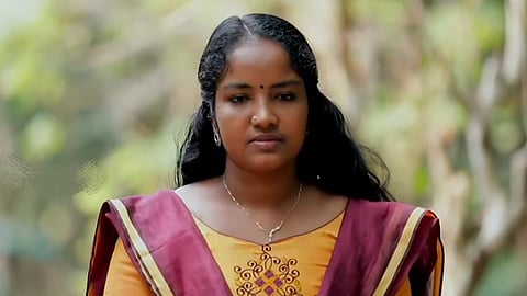 Image featuring Divya Johny wearing yellow traditional attire with a brown shawl.