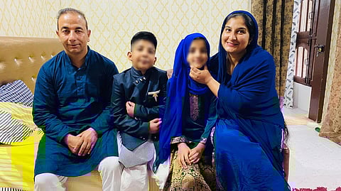 A picture of the family, dressed up for some festivity. Parents and the twins seated on a cot. 
