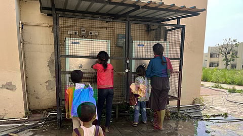 A group of children stand near a water dispenser in one of the camps in Jammu district. Their backs are turned to the camera, their faces hidden