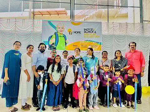 Group of adults and children smiling, holding umbrellas, with a “Back to School” banner behind