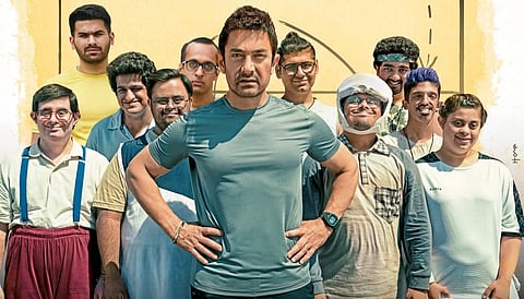 Aamir Khan stands with hands on hips, surrounded by a group of smiling young adults portraying athletes with intellectual disabilities, from the promotional poster of Sitaare Zameen Par.