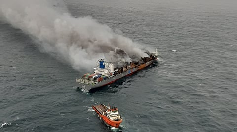 Aerial view of the Wan Hai 503 container ship on fire in the sea, with thick smoke rising and a smaller orange rescue vessel nearby.