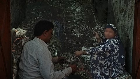 Two workers are seen manually stripping and sorting electrical wires inside a small room filled with coiled metal cables, likely as part of an informal recycling or scrap processing operation.