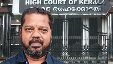 A stylised image with PK Suresh Kumar in the foreground and the Kerala High Court in the background. Suresh sports a beard and wears a blue shirt