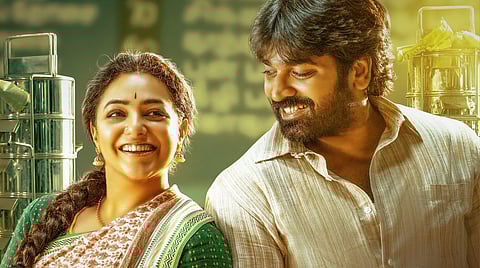 Vijay Sethupathi and Nithya Menen share a warm smile in a still from Thalaivan Thalaivii, standing close together in a sunlit kitchen setting with stacked steel tiffin carriers in the background.