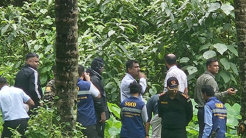 In a thick forest covered in vegetation, officials are seen examining the alleged burial sites
