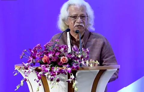 Adoor Gopalakrishnan delivering a speech at a podium decorated with flowers during the Kerala film policy conclave.