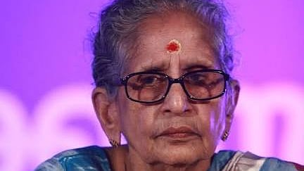 M Leelavathy, elderly Malayalam writer wearing a blue and white saree with glasses, sitting against a purple background.