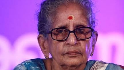 M Leelavathy, elderly Malayalam writer wearing a blue and white saree with glasses, sitting against a purple background.
