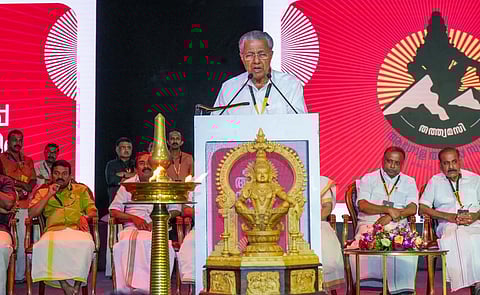 Kerala Chief Minister Pinarayi Vijayan speaks at the Global Ayyappa Sangamam, standing at a podium adorned with a golden idol of Lord Ayyappa, with dignitaries seated behind him on stage.