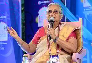 Sudha Murthy speaking at an event, mic in left hand, seated in a chair