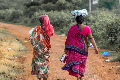 Two women in brightly coloured sarees walk along a dusty rural path surrounded by greenery, representing rural and tribal communities in India's eastern ghats whose lands are under threat.