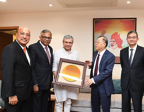 India's Minister for Railways, Communications, Electronics & Information Technology, Ashwini Vaishnaw (center, wearing white kurta), posing with four men, including N. Chandrasekaran (second from left, Chairman of Tata Sons) and two executives from Powerchip Semiconductor Manufacturing Corporation (PSMC), as they present a framed golden silicon wafer. The setting is an office with a large painting in the background featuring Prime Minister Narendra Modi.