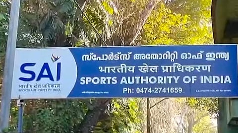 A blue signboard of the Sports Authority of India (SAI) displayed at the entrance of a campus, featuring the SAI logo along with the name written in Malayalam, Hindi, and English, with trees visible in the background.