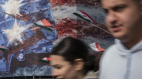 
Iranian youths walk past a building covered with a giant billboard depicting an image of the destroyed USS Abraham Lincoln. 