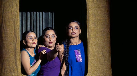 Three women look out from a window frame.