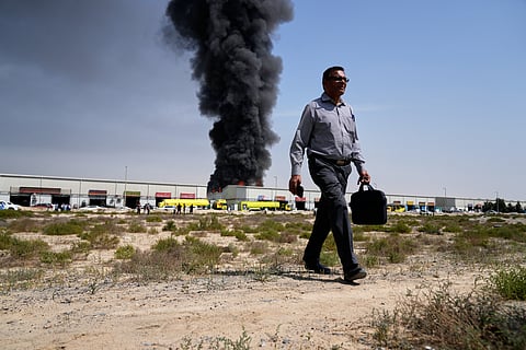 A man walks away after watching as a black plume of smoke rises from a warehouse in the industrial area of Sharjah City, United Arab Emirates, Sunday, March 1, 2026, following reports of Iranian strikes in Dubai. 