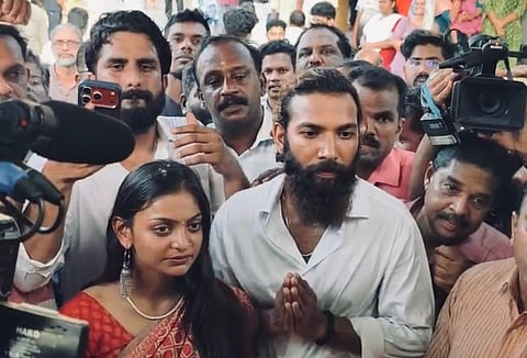 Monalisa Bhosle, wearing a red saree, stands beside Farman Khan as he folds his hands. The couple are surrounded by journalists with cameras and microphones and a crowd of onlookers in Thiruvananthapuram after their wedding in Vizhinjam.