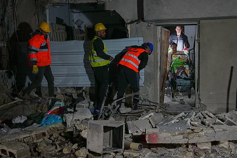 Residents carry personal belongings as they leave a building damaged in a missile strike in Tel Aviv, Israel, early Saturday, March 28, 2026. 