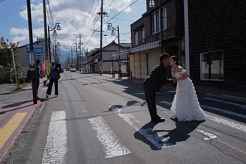 Foreign visitors pose for photos at Honcho Street with Mt. Fuji as background on Wednesday, April 8, 2026, in Fujiyoshida, west of Tokyo. (AP Photo/Eugene Hoshiko)

