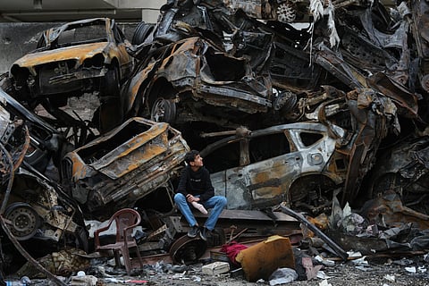 A man sits next to charred cars and wreckage where a building was destroyed by an Israeli airstrike the previous Wednesday, in central Beirut, Lebanon, Tuesday, April 14, 2026. (AP Photo/Hassan Ammar)

