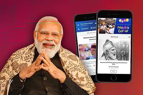 Prime Minister Narendra Modi smiling, his hands folded near his face, the NAMO app can be seen behind him