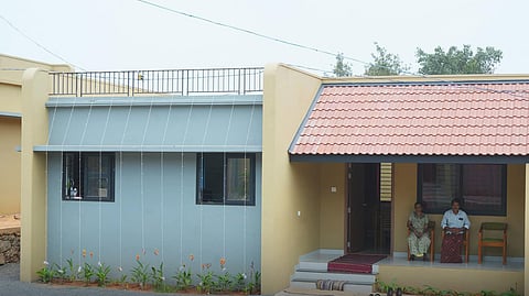 Newly built house by IUML for Wayanad landslide survivors, featuring a single-storey design with tiled roof and a small front porch where two residents are seated.