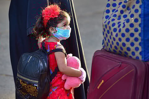A child wearing a mask waits in a queue with her family members to board a special train.