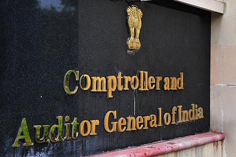 A golden sign on a black marble wall that reads "Comptroller and Auditor General of India" in 3D lettering. Above the text is the State Emblem of India (the Lion Capital of Ashoka) in gold. The sign is mounted on an exterior building wall with a pinkish stone ledge at the bottom.