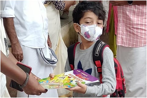 Child receiving a book on school reopening day in Kerala