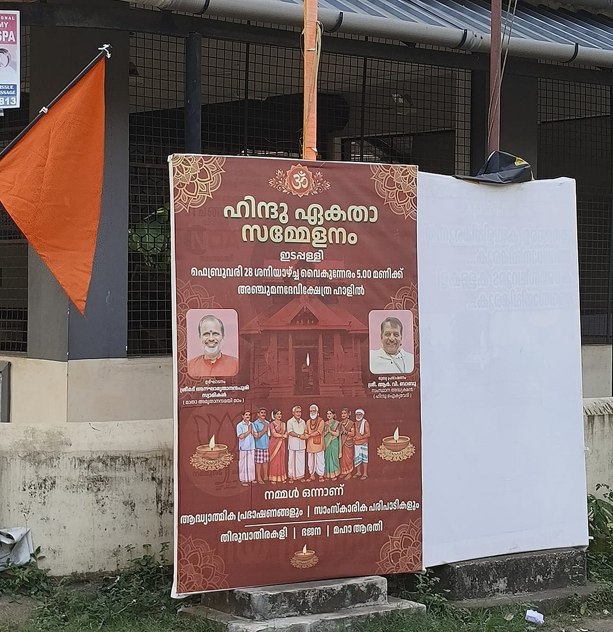 Poster announcing a “Hindu Ekta Sammelanam” displayed beside a saffron flag on a roadside wall.